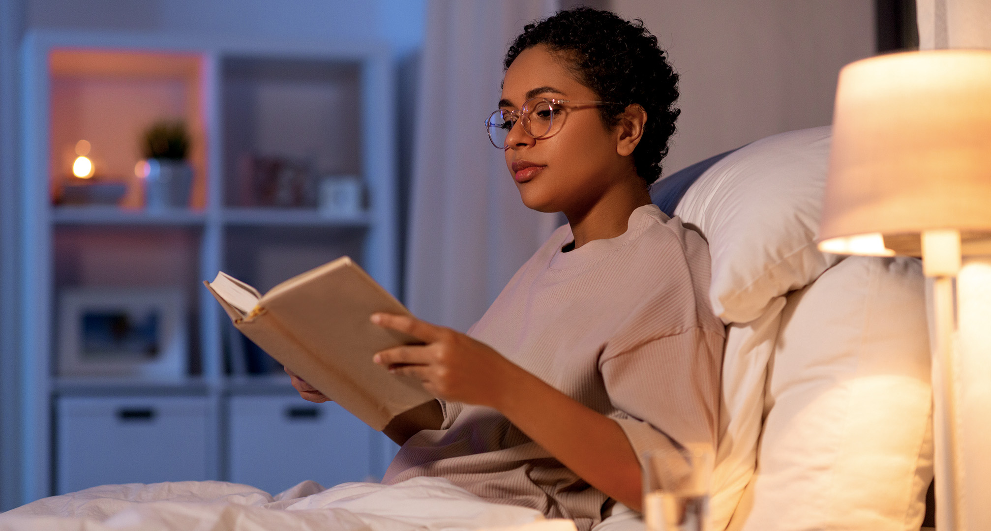 persona con gafas y leyendo un libro en una habitación poco iluminada